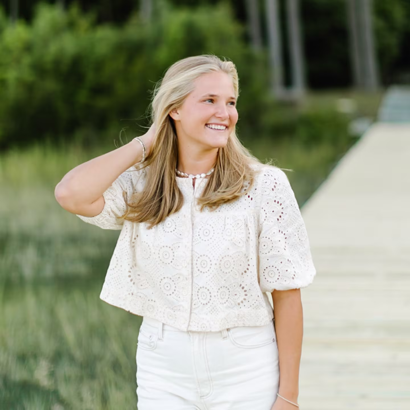 Lightweight white eyelet blouse with textured pattern, styled outdoors with soft greenery background