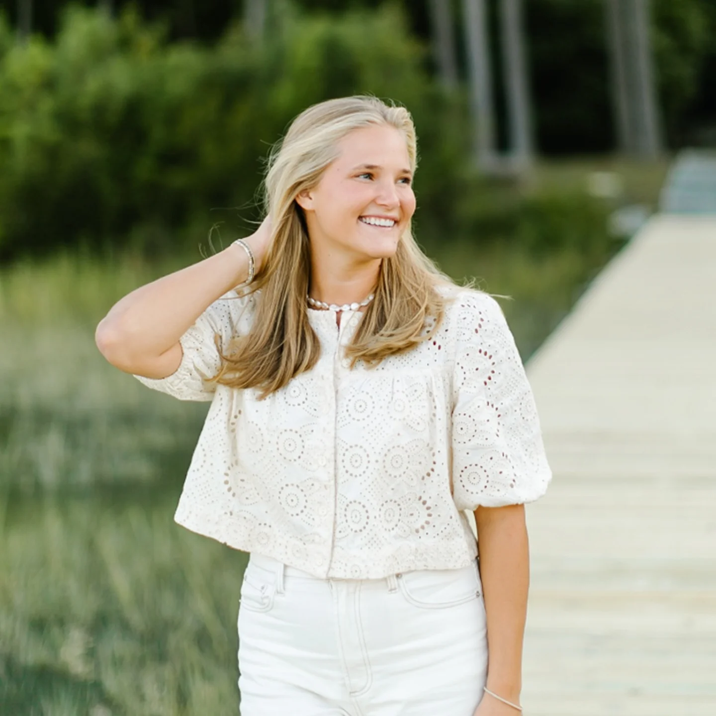 Lightweight white eyelet blouse with textured pattern, styled outdoors with soft greenery background