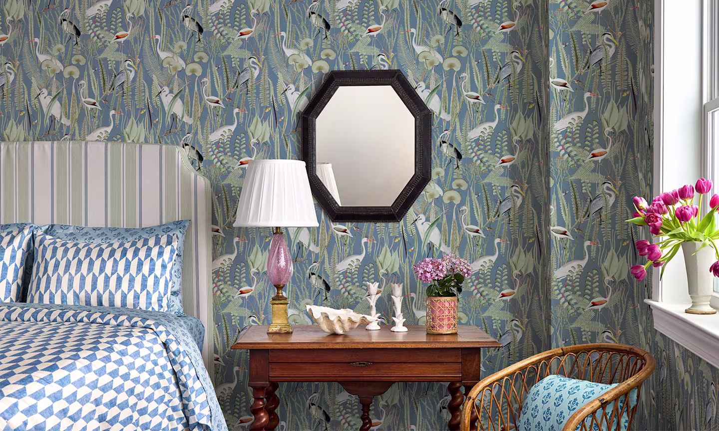 Bedroom with coastal heron wallpaper a striped headboard and geometric blue and white bedding.