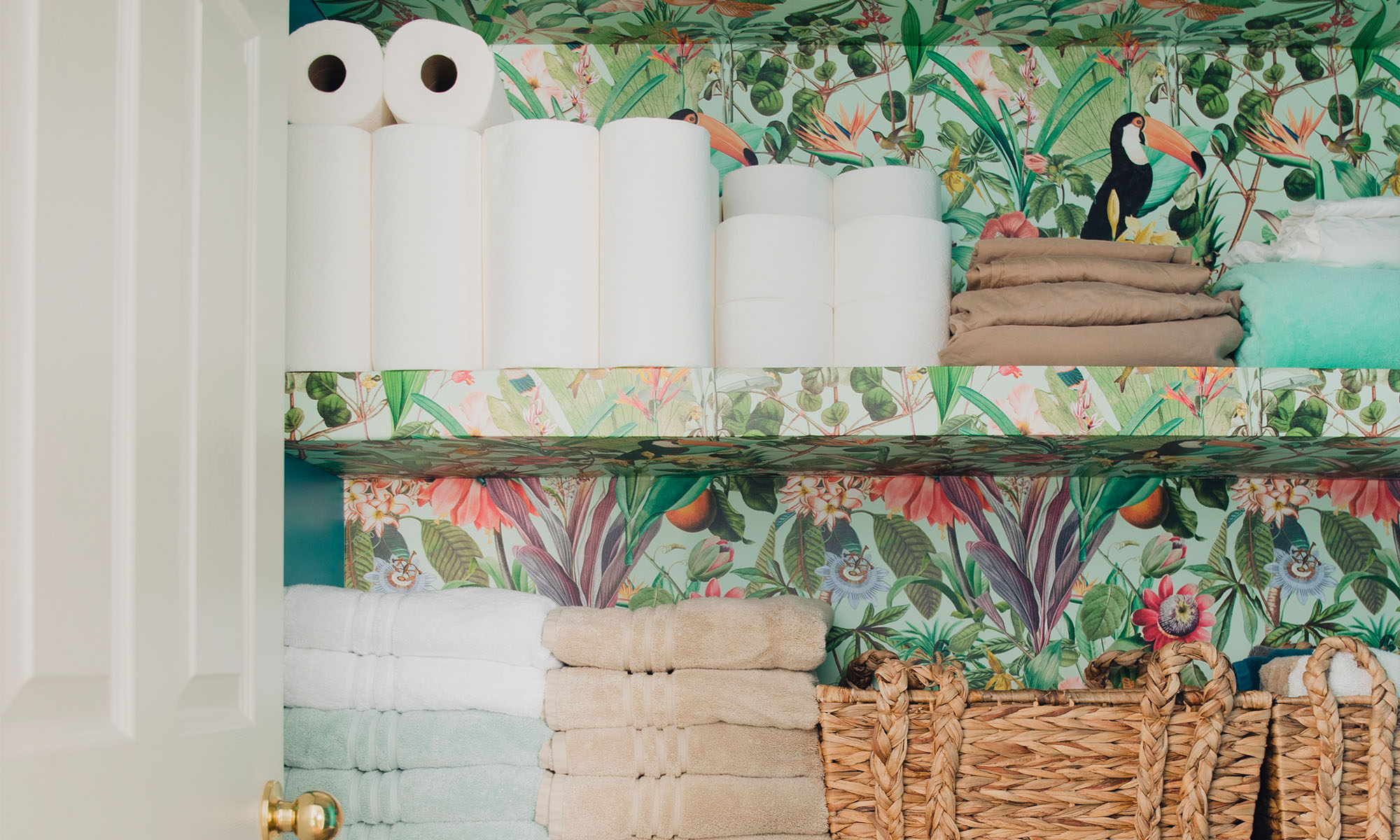 A bathroom closet wallpapered with a tropical inspired wallpaper.