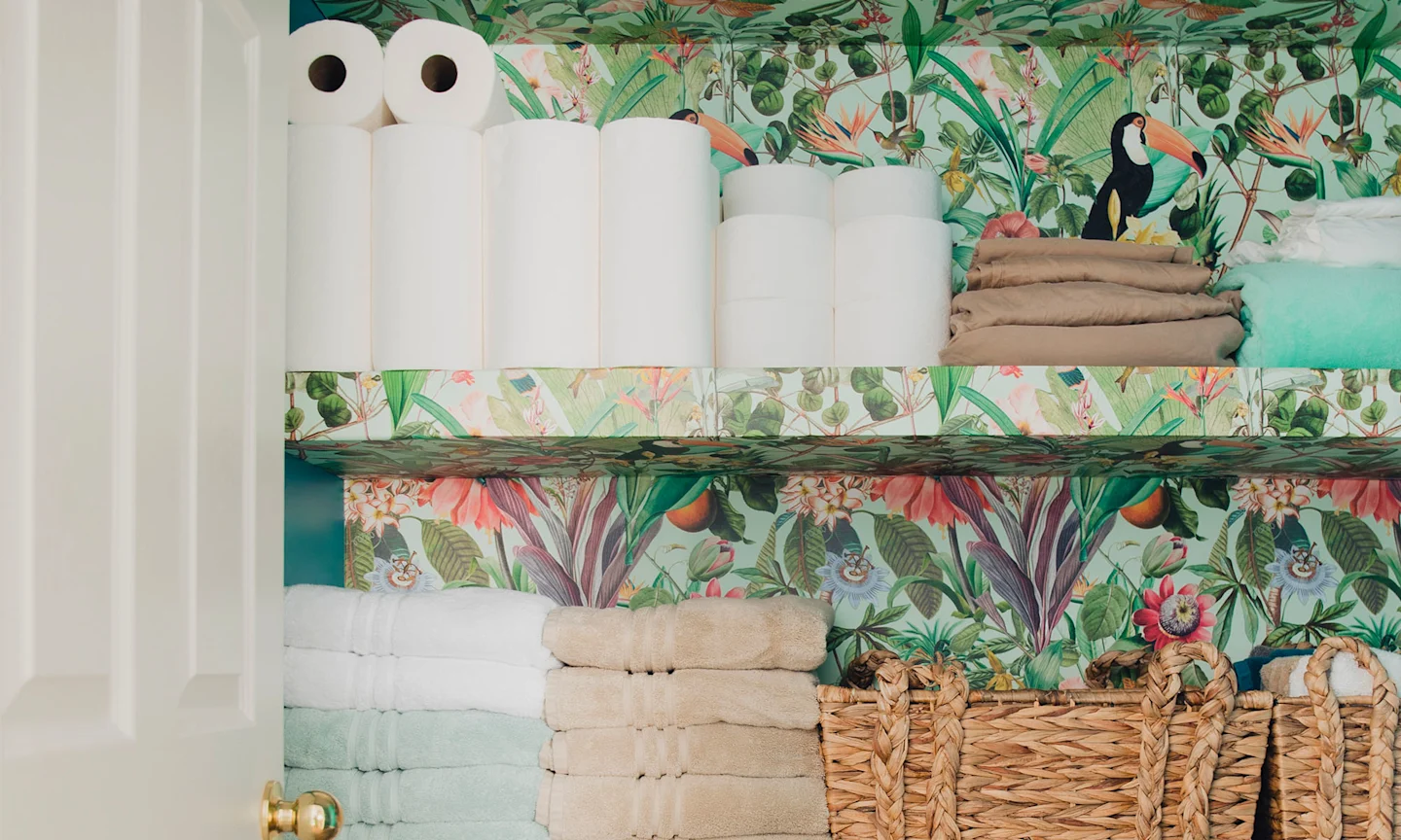 A bathroom closet wallpapered with a tropical inspired wallpaper.
