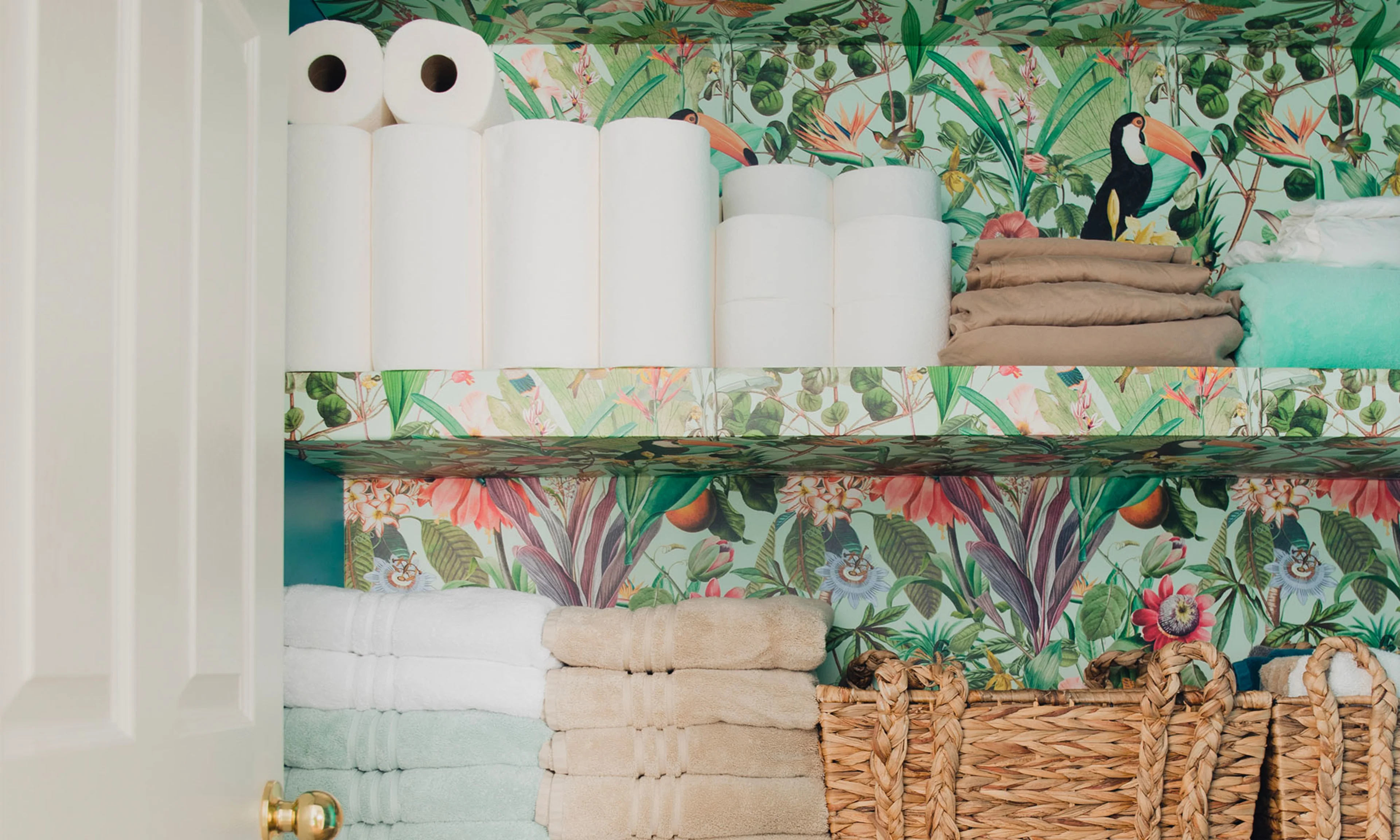 A bathroom closet wallpapered with a tropical inspired wallpaper.
