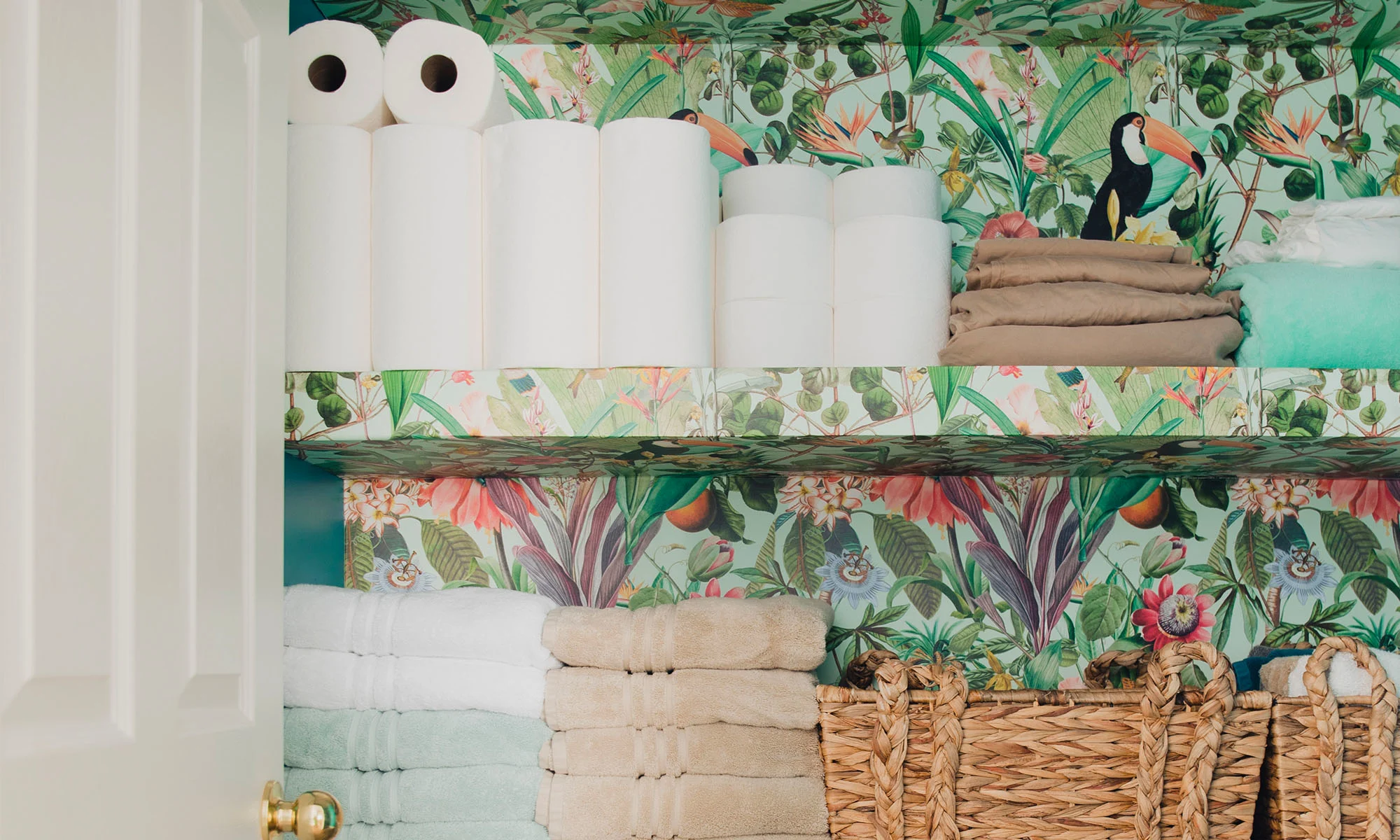 A bathroom closet wallpapered with a tropical inspired wallpaper.