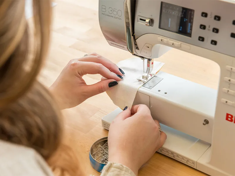 A woman is stitching one side of the baby shoe heel one side of the baby shoe toe piece.