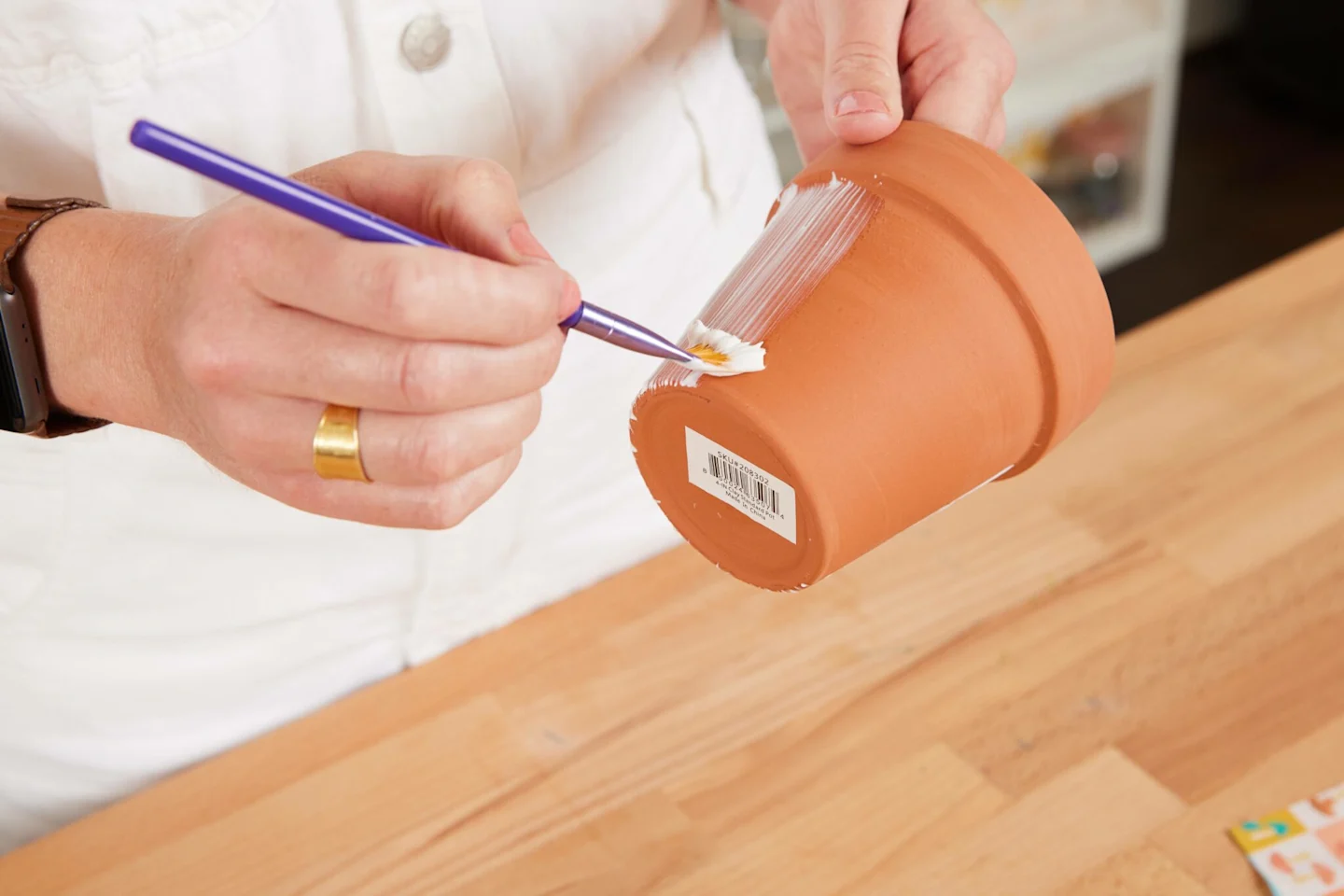 Alexa uses a paintbrush to liberally cover the terracotta pot with Mod Podge Outdoor. The glue paints on white, but will eventually dry clear.