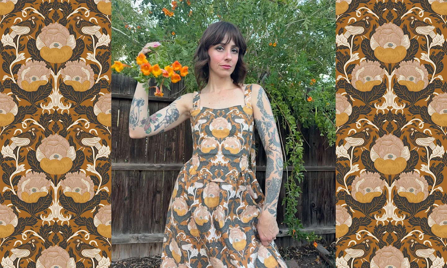 a women in a sleeveless dress, standing agains a wooden fence. She is holding a blossoming tree branch.