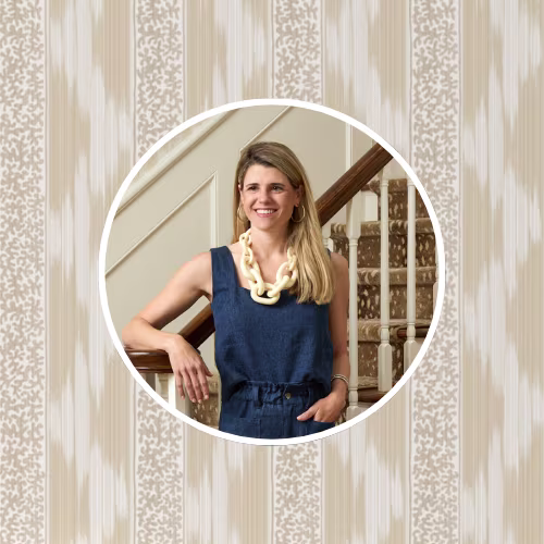 Woman standing by a staircase, wearing a navy sleeveless outfit and a chunky necklace, with one arm resting