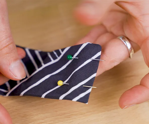 Two sewing pins have been placed on the short top end of a hanging rod tab. The design on the fabric is navy with white lines.