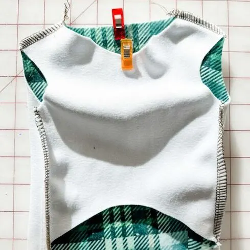 The front bodice piece is laying design side down on top of the back bodice piece, which is design side up. One sewing clip is in the top center of each piece of fabric. Stitches on the shoulders and sides of the bodice indicate what it should look like a