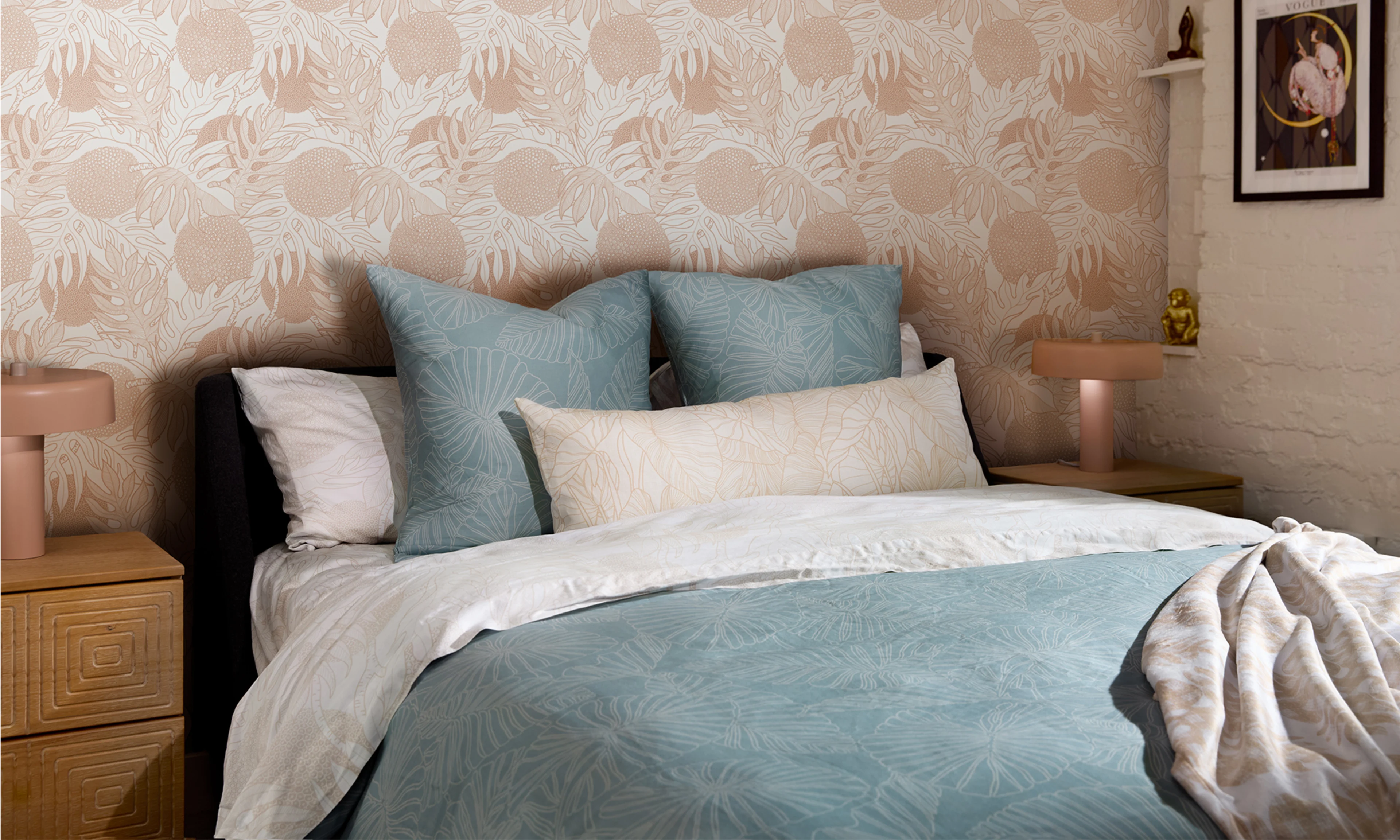 A bed with a soft blue and beige duvet cover with a neutral peach wallpaper accent wall.