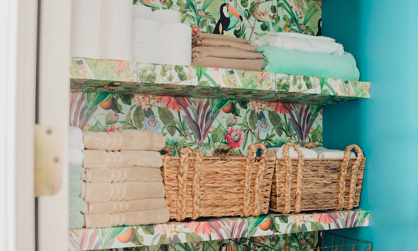 A bathroom closet wallpapered in tropical inspired wallpaper.