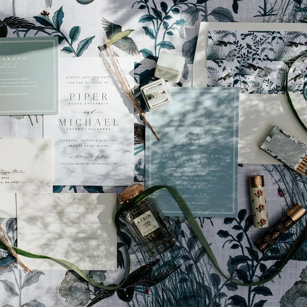 Wedding invitations on top of a blue floral fabric tablecloth.