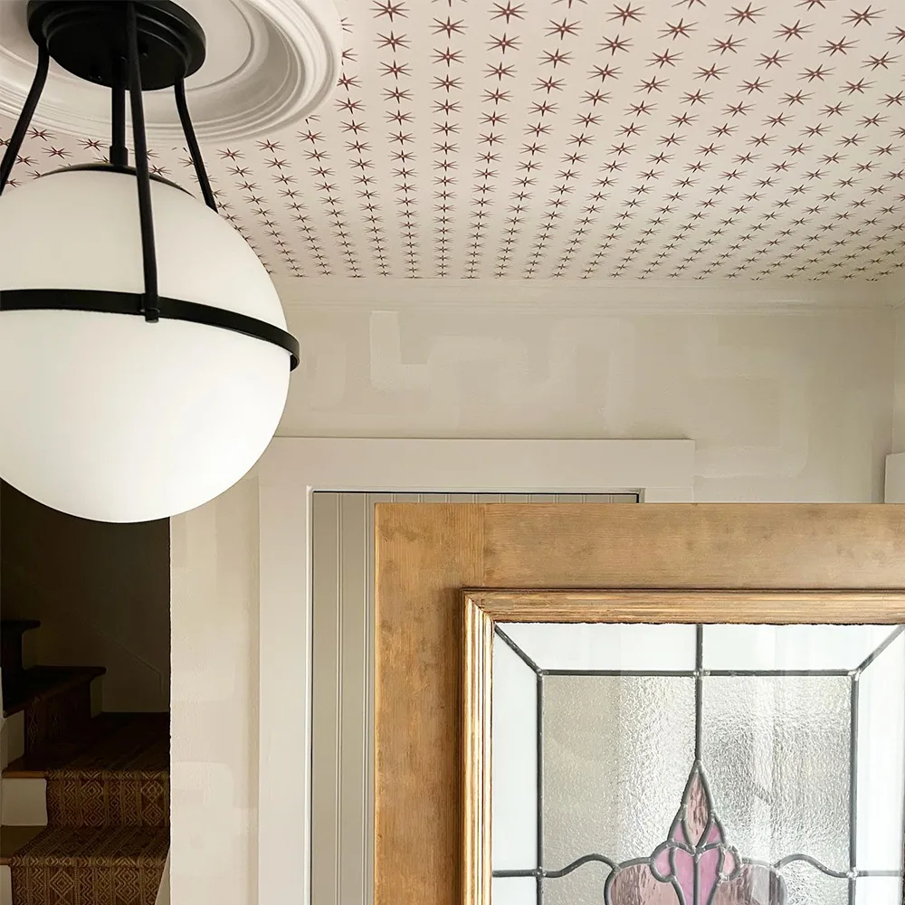 Brown stars on cream wallpaper hanging on a ceiling in an entryway.