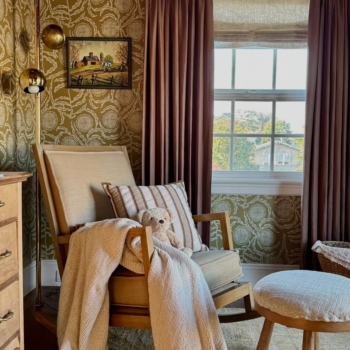 Rocking chair with teddy bear and green floral wallpaper in background