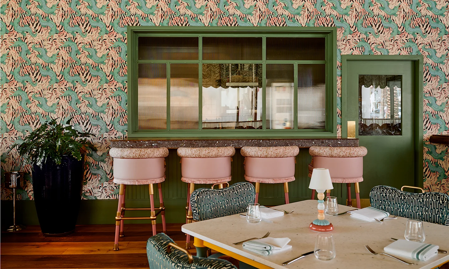 Bar Issi with maximalist gator wallpaper, pink bar stools and a dining table.