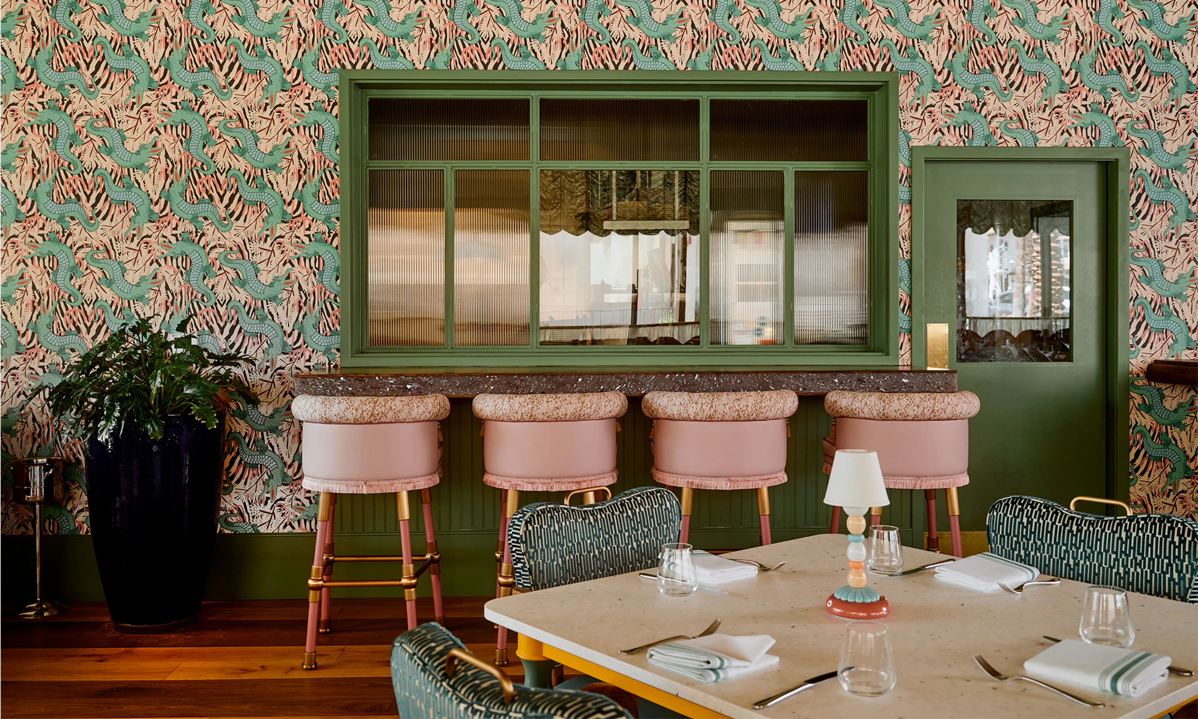 Bar Issi with maximalist gator wallpaper, pink bar stools and a dining table.