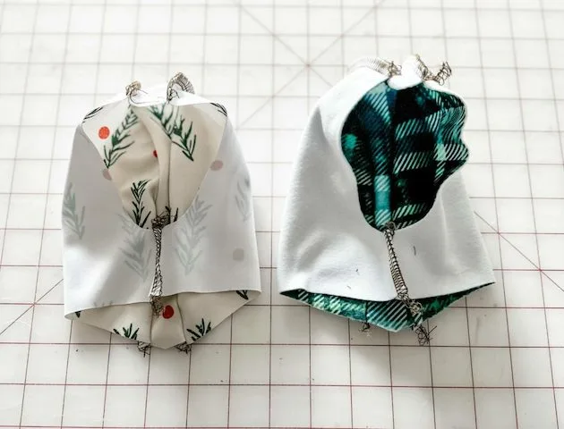 Two parts of the dog coat’s hoodie, the exterior and the interior lining, lay on a grid surface with the fabric’s wrong side facing out. The fabric lays on a white cutting mat with a red grid.