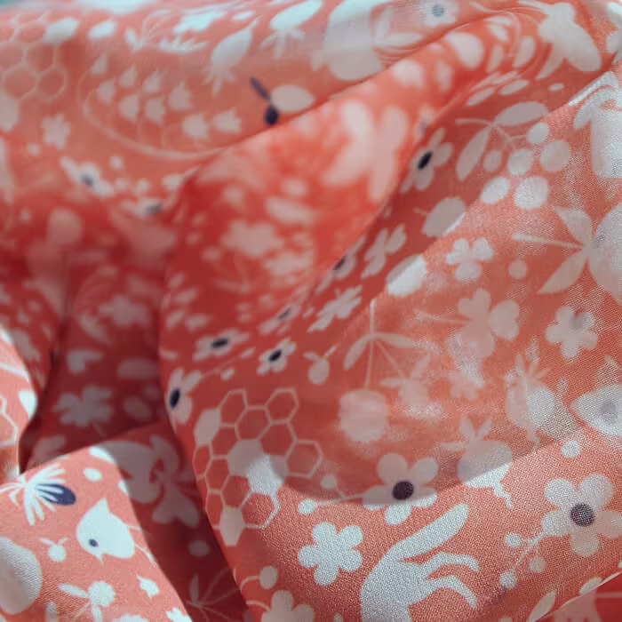 Close-up of flowing coral-colored fabric with a white floral and nature-inspired pattern.