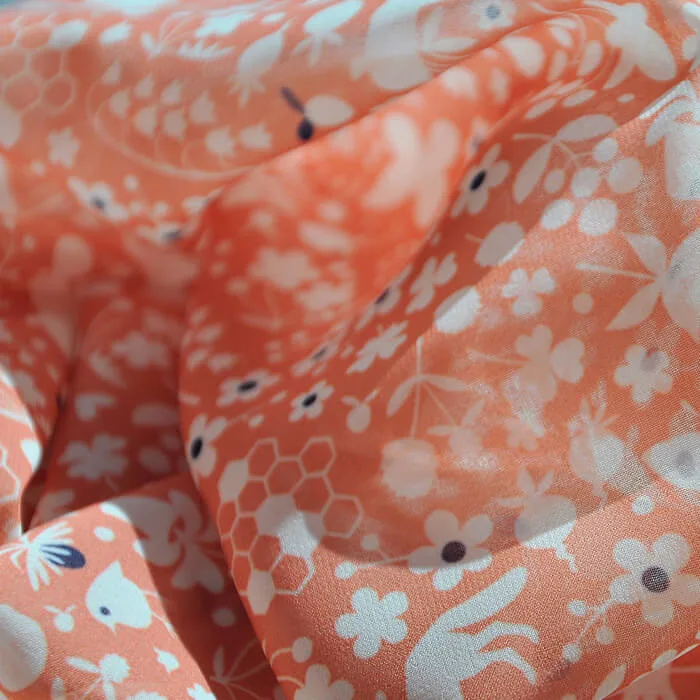 Close-up of flowing coral-colored fabric with a white floral and nature-inspired pattern.