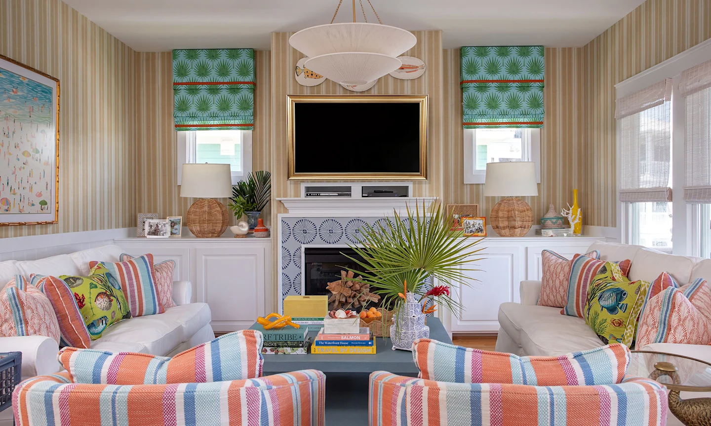 Living area with tan striped wallpaper botanical curtains and summery pillows.