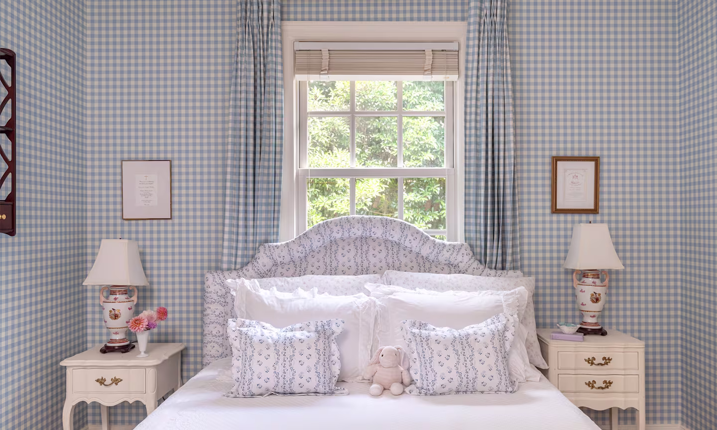 Bedroom with blue gingham wallpaper and curtains and striped floral headboard and pillows.