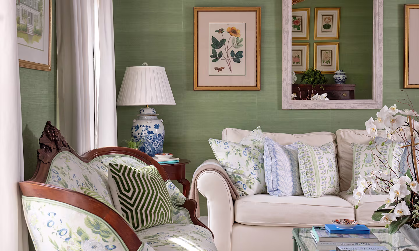 Living room with textured green wallpaper a floral upholstered settee and coordinating blue and green throw pillows.
