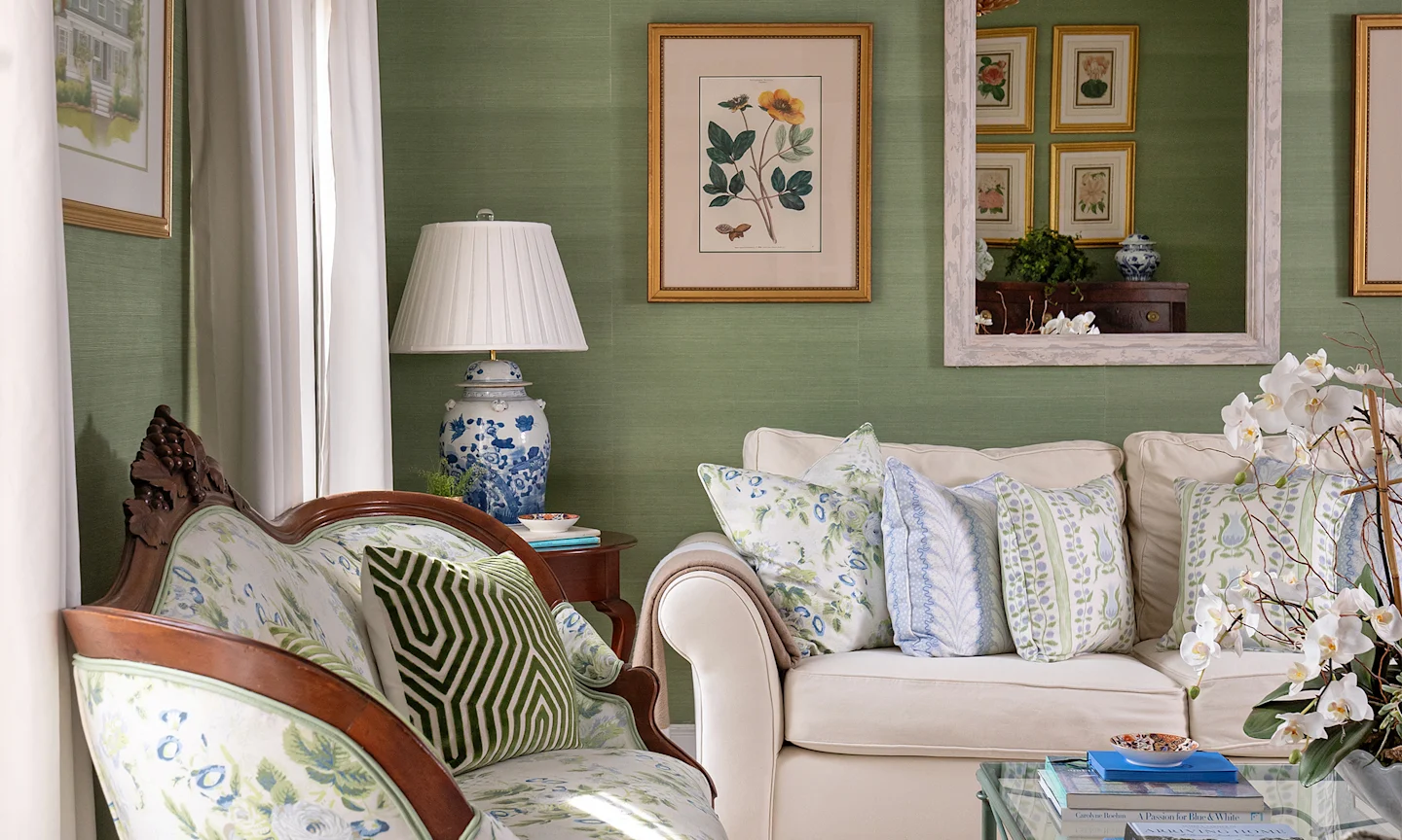 Living room with textured green wallpaper a floral upholstered settee and coordinating blue and green throw pillows.