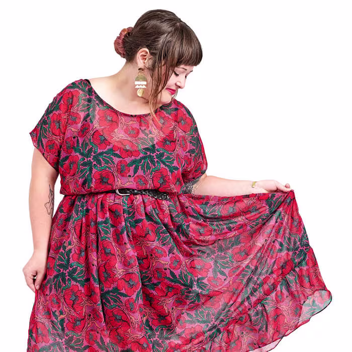 Person wearing a red dress with a bold floral pattern, holding out part of the skirt to show the fabric.