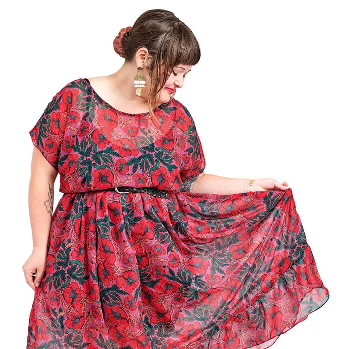 Person wearing a red dress with a bold floral pattern, holding out part of the skirt to show the fabric.