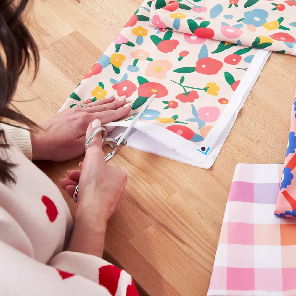 Woman cutting floral cotton fabric with scissors