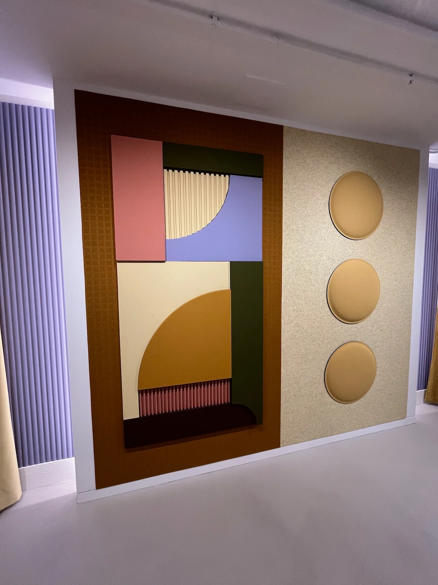 Geometric acoustic wall panels in layered shapes and warm neutral tones, paired with round upholstered panels in a modern interior display