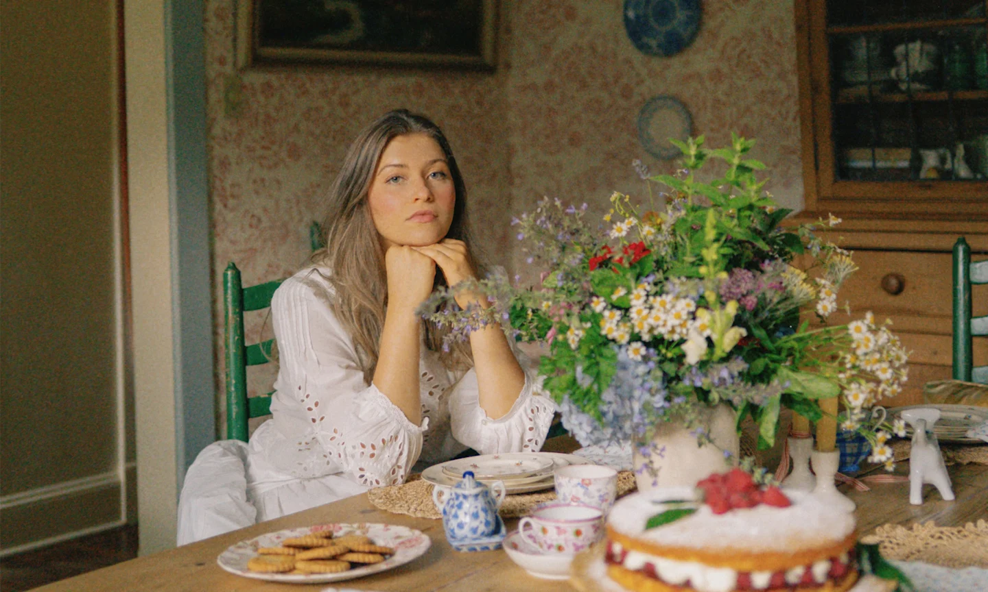 Headshot of Margo Roth at her dining room table that is filled with china, baked goods and flowers.