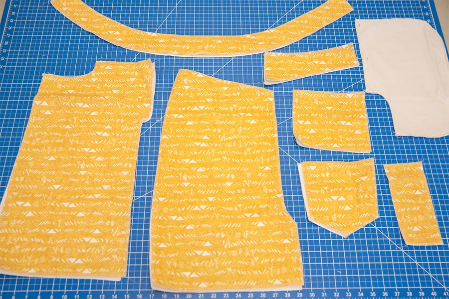 Yellow pieces of fabric to make a denim skirt lay on a blue work station.
