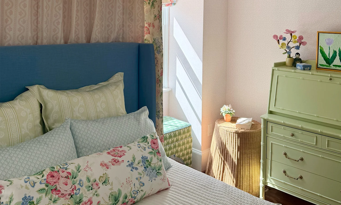 Girls bedroom with pink wallpaper blue and green pillows on a bed with a matching fabric canopy and green furniture.