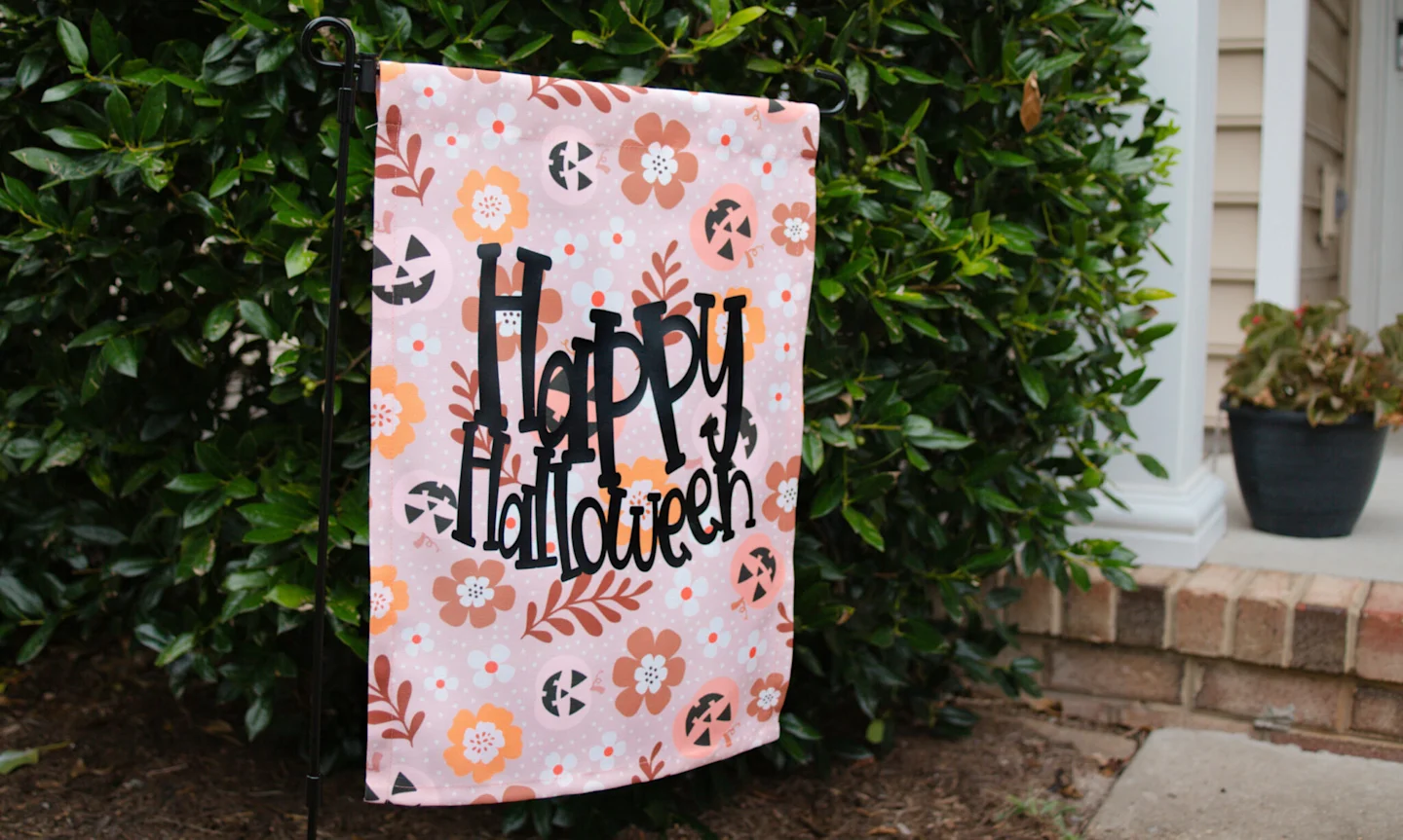 Finished Halloween garden flag, reading "Happy Halloween" in black fun text and sitting in the garden.