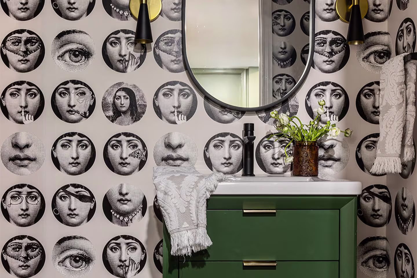 Whimsical bathroom featuring wallpaper with faces in mirrors and a green sink cabinet.