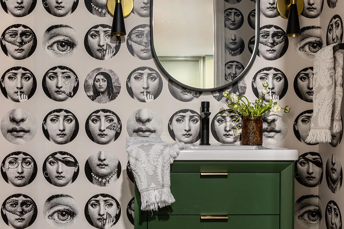Whimsical bathroom featuring wallpaper with faces in mirrors and a green sink cabinet.