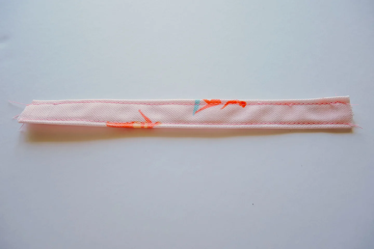 A small rectangle of fabric has been sewn along the top edge and the bottom edge. The fabric features a design with small female surfers surfing through a pink background.
