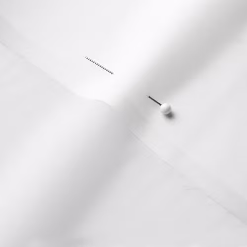 A close-up photo of white fabric with a pin running through it