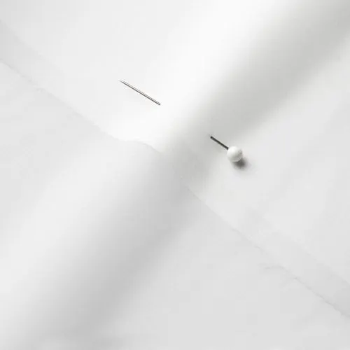 A close-up photo of white fabric with a pin running through it