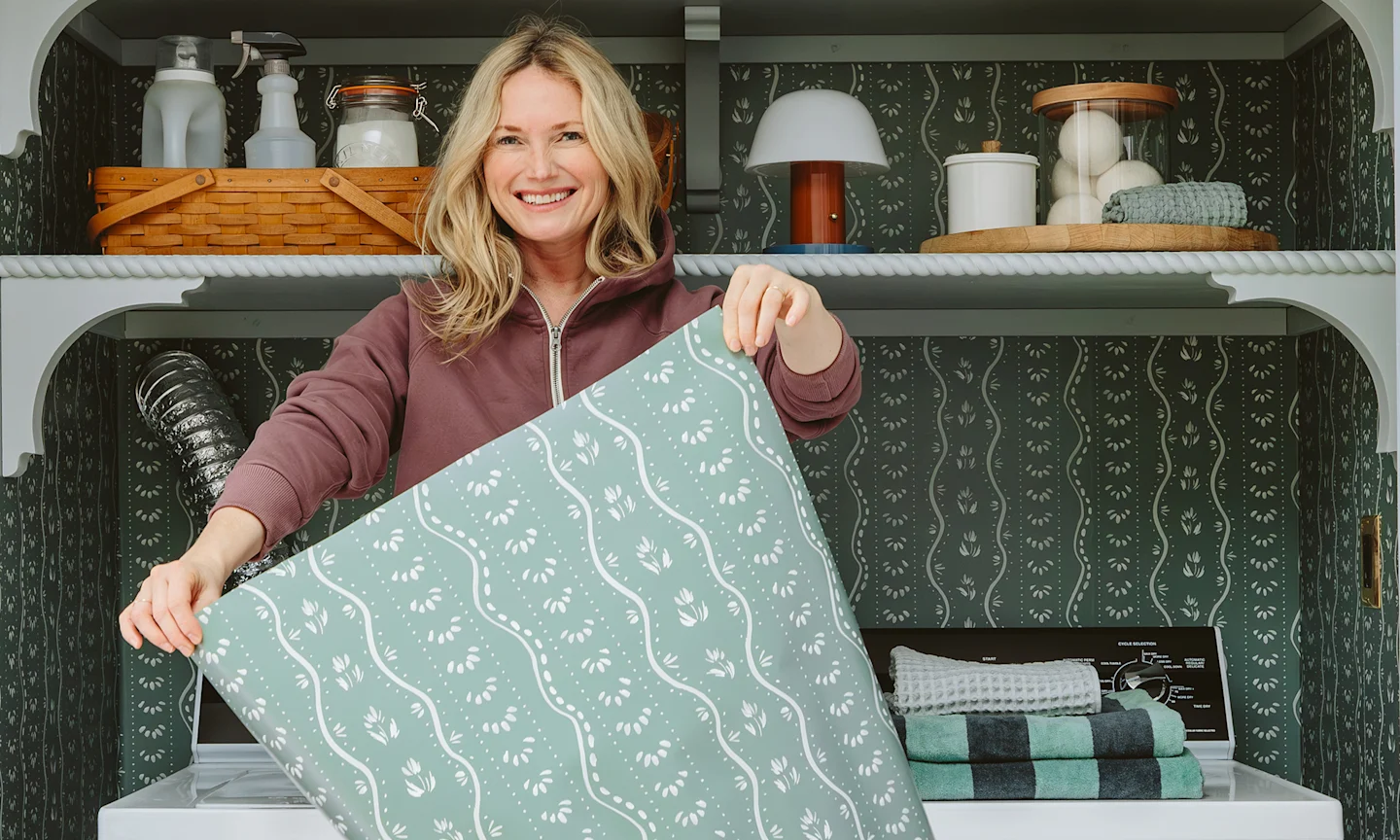 Emily Henderson holding up Pre-Pasted wallpaper in a teal-grey stripe design.
