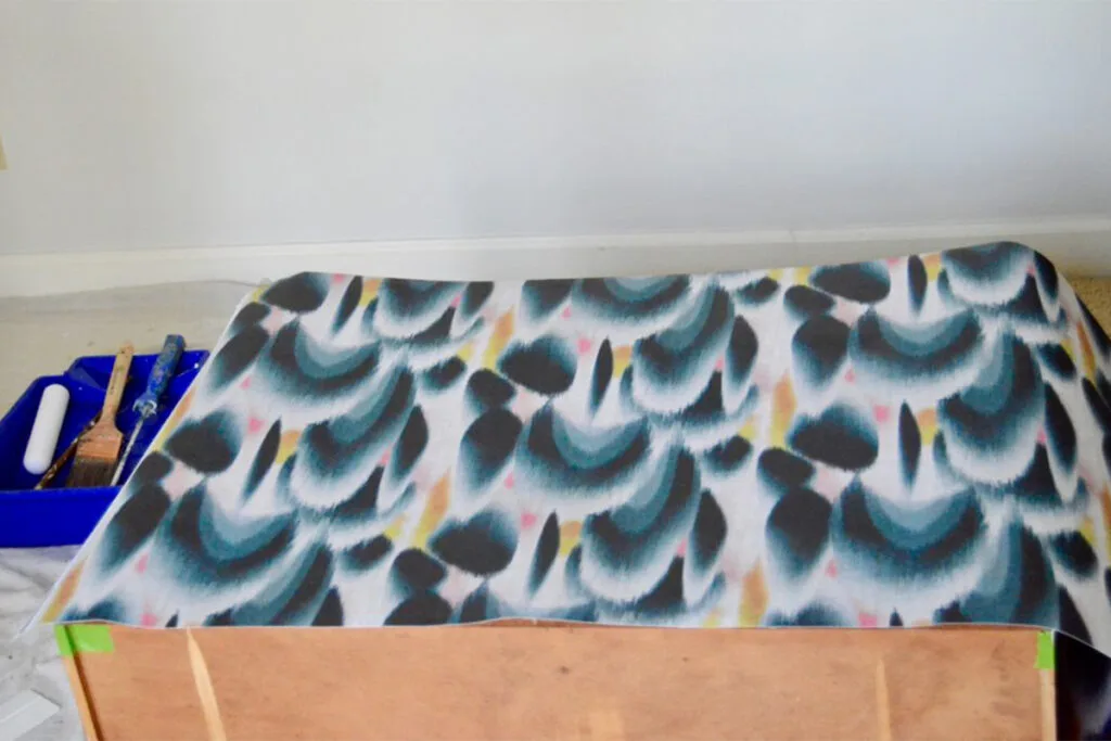 A roll of wallpaper lays across a dresser drawer that is facing upward.