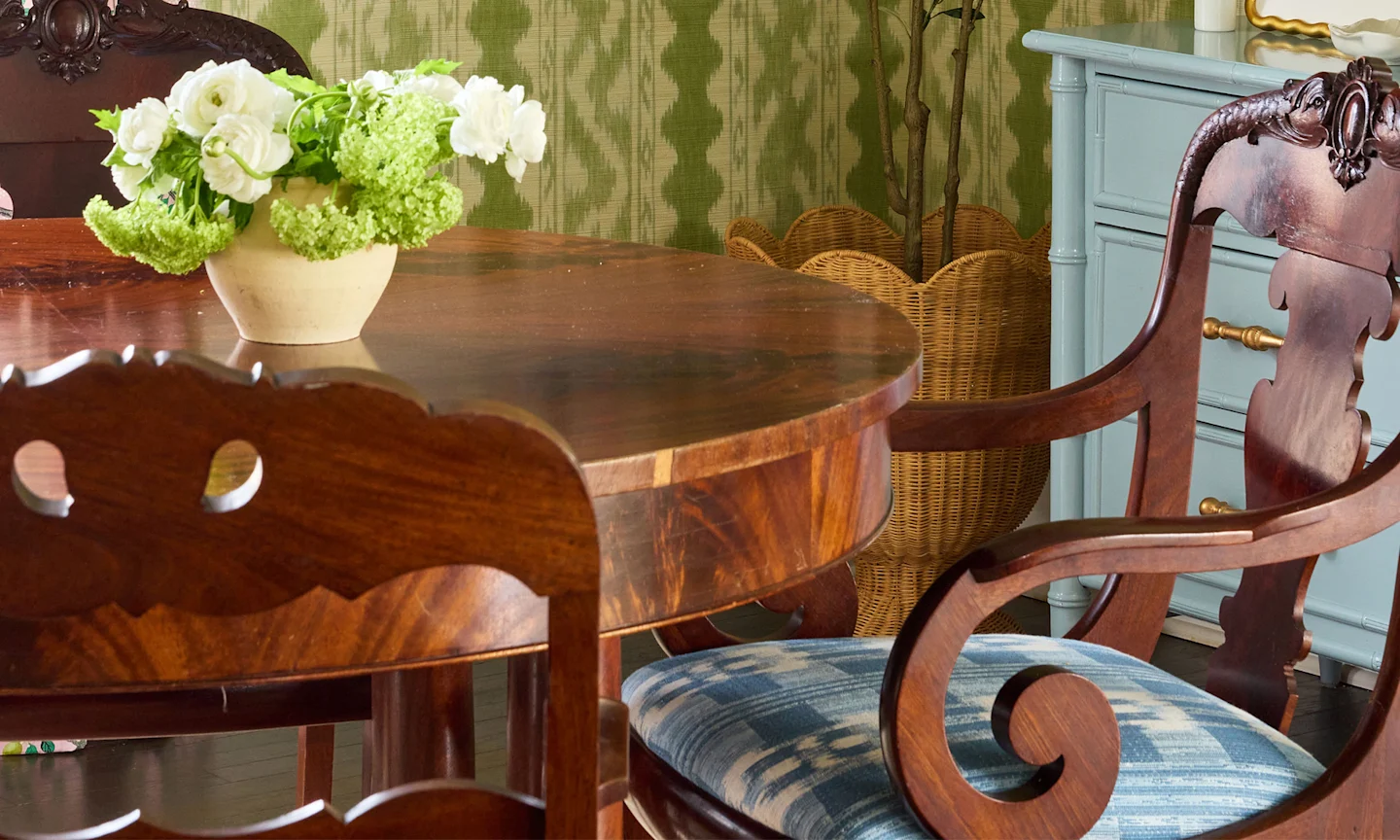 Dining table and chair with blue upholstered seat and green striped wallpaper.