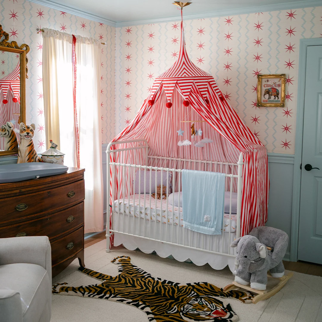 Nursery featuring red-and-white striped crib canopy, star-pattern wallpaper, vintage circus decor, and animal-themed accents.