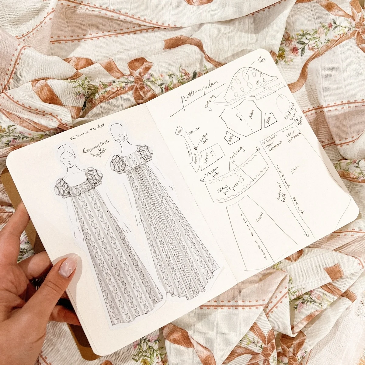an opene sketch book rests on gently-wrinkled gauze fabric in a pretty ribbon bow design