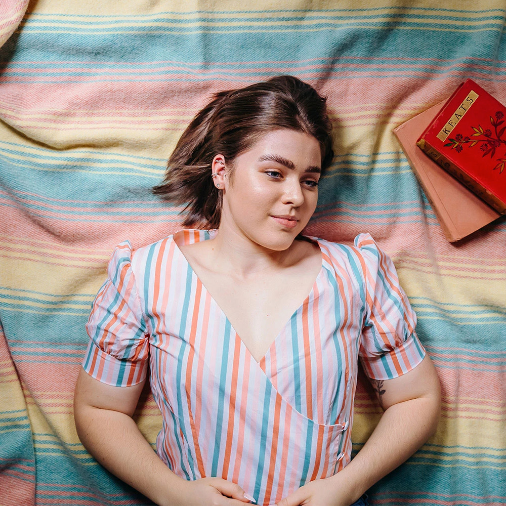 Woman wearing a pink and blue striped blouse while laying on a picnic blanket.