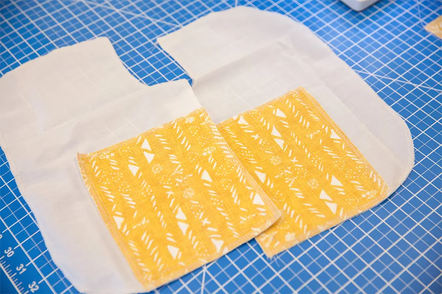 Two denim yellow squares rest on fabic lining on a blue work station.