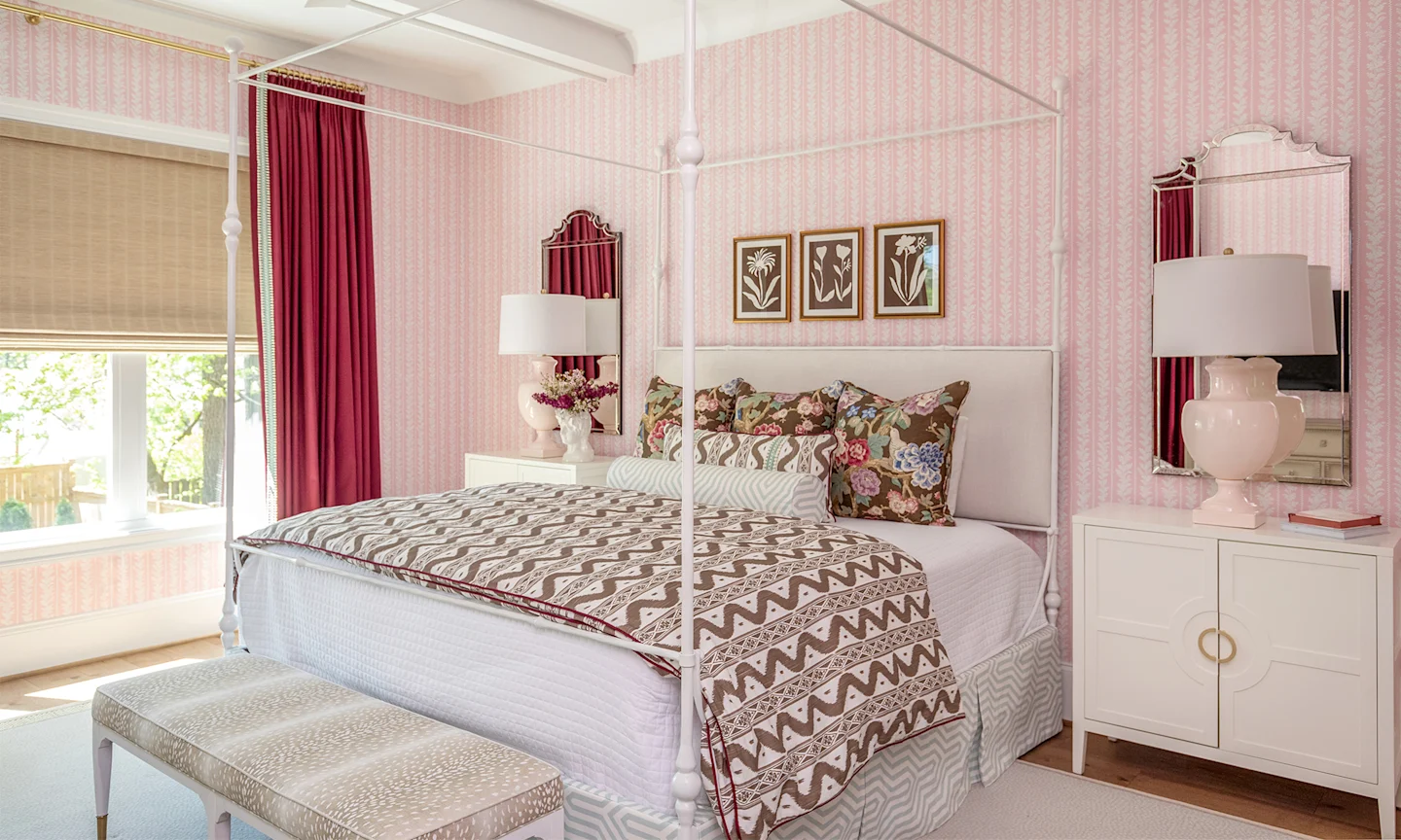 Bedroom with pink striped wallpaper and a four poster bed with a whimsical striped duvet cover and floral pillows.
