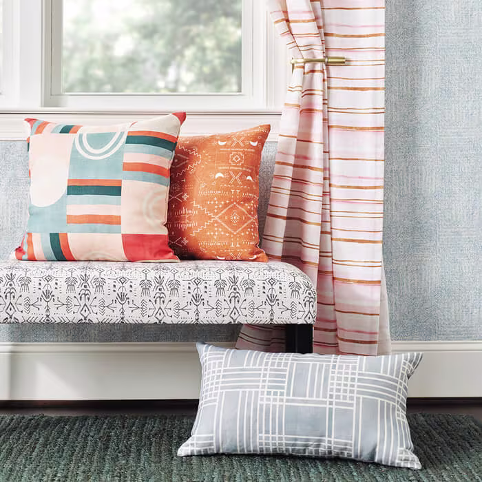 Styled interior scene with patterned throw pillows on a bench, a striped curtain pulled to the side, and a geometric lumbar pillow on the floor.