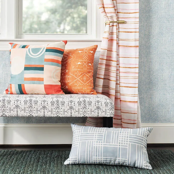 Styled interior scene with patterned throw pillows on a bench, a striped curtain pulled to the side, and a geometric lumbar pillow on the floor.